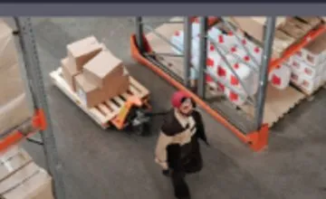 Warehouse aisle camera view with a worker moving a pallet
