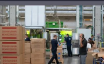 Packing area camera view with staff and stacked boxes